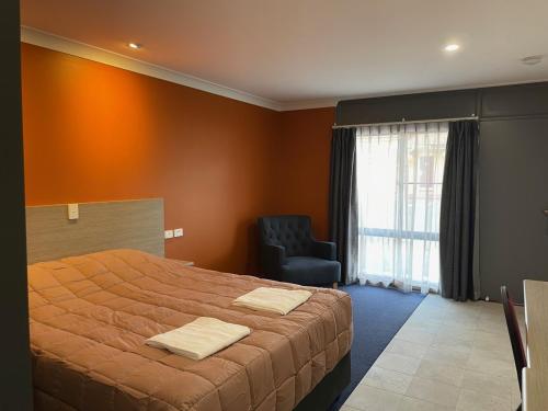 een slaapkamer met een groot bed en een stoel bij Homestead Motel in Dubbo