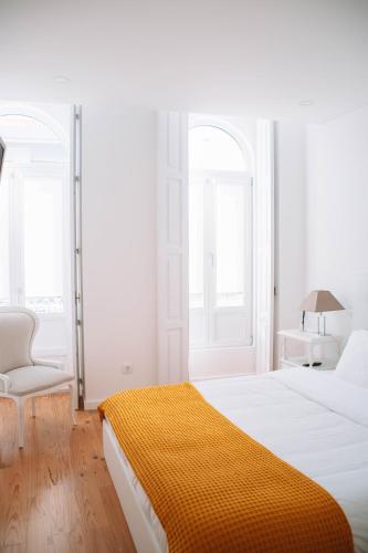 a white bedroom with a large bed and a chair at Just Like Home - Casinha da Vila em Caminha in Caminha