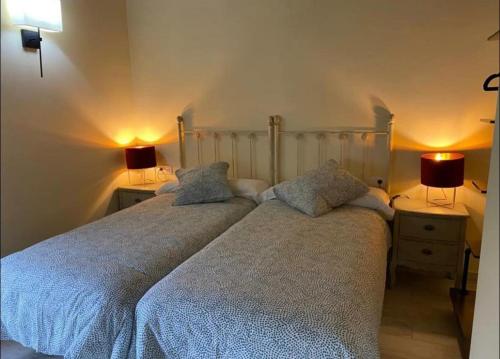 two beds in a bedroom with two lamps on tables at BUNGALOW LA COCINA in Valdaliga 