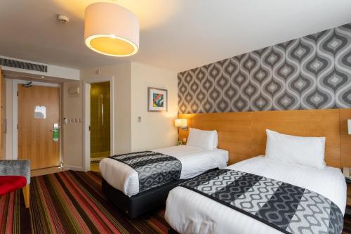 a hotel room with two beds and a red chair at Holiday Inn Newcastle-Jesmond by IHG in Newcastle upon Tyne