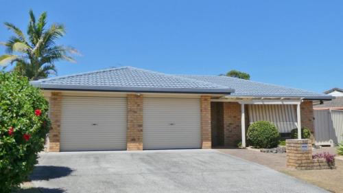 a house with white garage doors in a driveway at 25 Admiralty Court, Yamba in Yamba