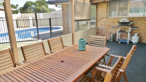 a wooden table and chairs on a patio with a pool at 25 Admiralty Court, Yamba in Yamba