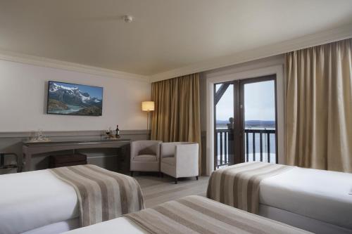 a hotel room with two beds and a balcony at Hotel Costaustralis in Puerto Natales