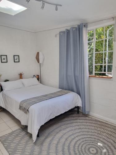 a white bedroom with a bed and a window at Sunlight Cottage in Cape Town