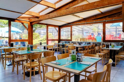 un restaurante con mesas, sillas y ventanas en Team Holiday - Camping de l'Etang du Pays Blanc, en Guérande