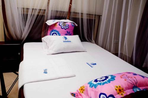 a bed with white sheets and a flower patterned pillow at Mujjo Hotel Kajjansi in Kampala
