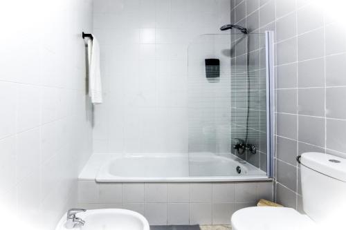 La salle de bains blanche est pourvue d'une baignoire et de toilettes. dans l'établissement Apartamento San Juan, à El Puerto de Santa María