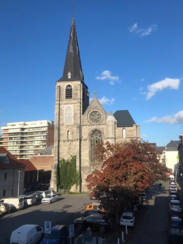 a church with a steeple and cars parked in a parking lot at Appartement centre ville in Tournai