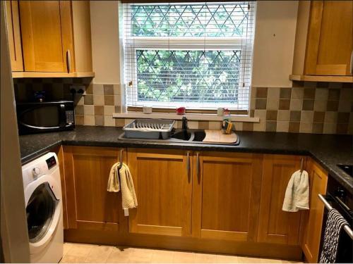 cocina con armarios de madera, fregadero y ventana en Lovely one-bed condo with free parking on premises, en Sunderland