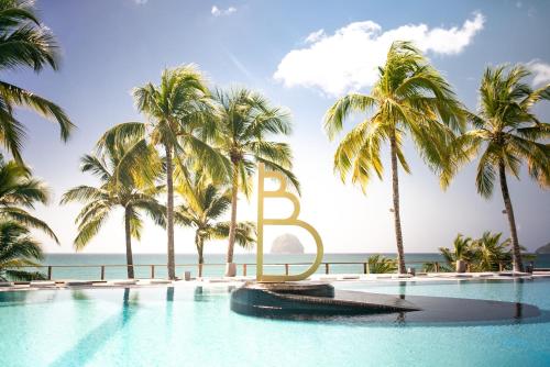 a pool with palm trees and a large letter b at KAY TI'TINY T2 NEUF de STANDING MER & PISCINE in Le Diamant