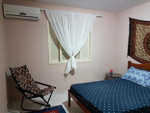 a bedroom with a bed and a chair and a window at Linda casa c/Piscina, Ar e conforto próximo do Mar in Itapoa