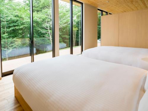 Rakuten STAY VILLA Aso Kurokawa -102 1LDK Capacity of 6 persons في ميناميوغوني: سريرين في غرفة نوم مع نوافذ كبيرة