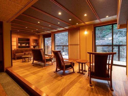 uma sala de estar com cadeiras, uma mesa e janelas em Shima-Onsen Toshimaya em Nakanojo