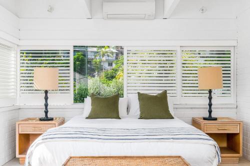 a white bedroom with a bed and two lamps at Baywatch at Wategos in Byron Bay