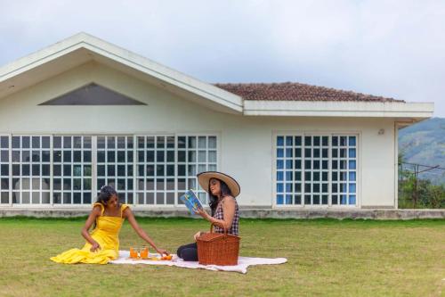 duas mulheres sentadas na relva em frente a uma casa em StayVista's Shivom Villa 12 - A Serene Escape with Views of the Valley and Lake em Lonavala