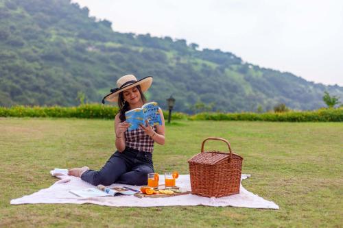 a woman sitting on a picnic blanket holding a book at StayVista's Shivom Villa 12 - A Serene Escape with Views of the Valley and Lake in Lonavala