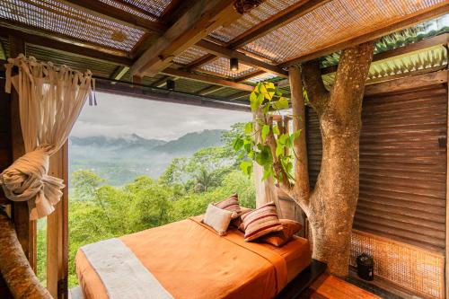 a bed in a room with a tree at Bird Hills Bamboo House in Karangasem