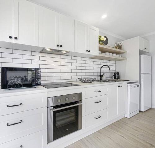 a white kitchen with white cabinets and an oven at Studio Seaside Self-contained apartment in Marcoola