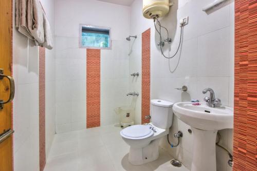 a white bathroom with a toilet and a sink at Ayushman Hotels in Manāli