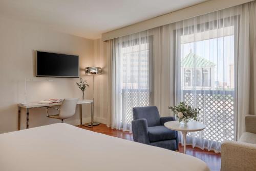 a hotel room with a bed and a desk and a window at NH Málaga in Málaga