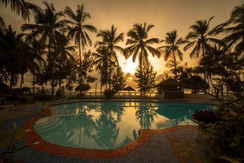 a pool with palm trees in front of a sunset at F-Zeen Boutique Hotel Zanzibar in Uroa