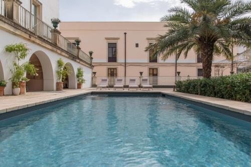 a swimming pool in front of a building with palm trees at Relais Monastero Santa Teresa - Albergo Diffuso in Nardò