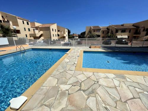 une grande piscine avec une passerelle en pierre à côté de certains bâtiments dans l'établissement charmand studio en résidence avec piscine, à Bandol