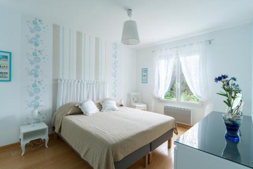 a white bedroom with a bed and a window at Le Chemin Vert - maison avec piscine in Matignon