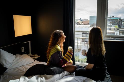 two women sitting on a bed looking out a window at Kip Hotel in London