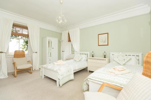 a white bedroom with two beds and a chair at The Corran in Lochgilphead