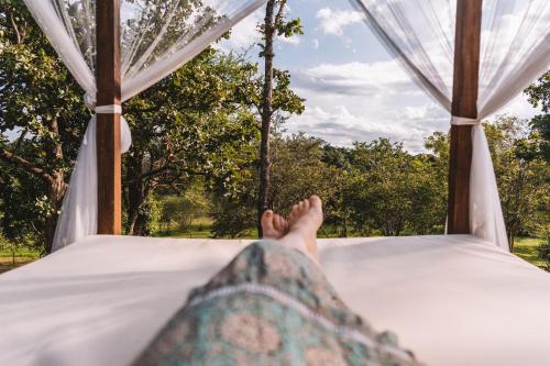 a persons legs laying on a bed looking out at trees at Ahaspokuna by Eco Team in Belihul Oya
