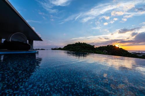 読谷村にあるグランディスタイル 沖縄 読谷 ホテル ＆ リゾートの夕日を背景に見えるスイミングプール