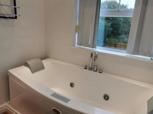 a white bath tub in a bathroom with a window at Luxury Tranquil Cottage with Hot tub, Log burner and Jacuzzi Bath in Alford