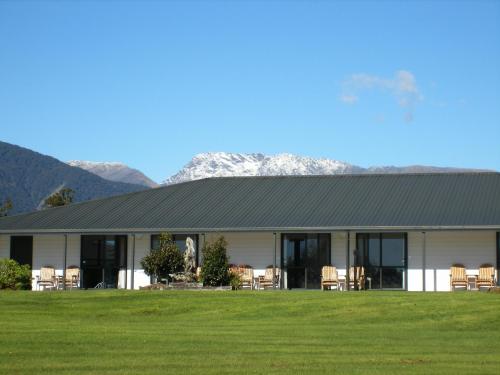 a large white building sitting in the middle of a grassy field at Heritage Park Lodge in Haast