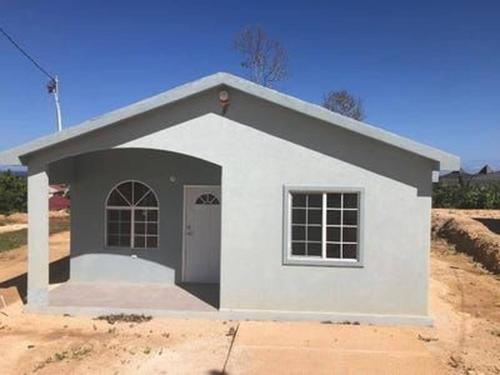 a small white house with a door in a field at Escape to Paradise Brand New Bungalow with Ocean View in Discovery Bay 1 in Discovery Bay