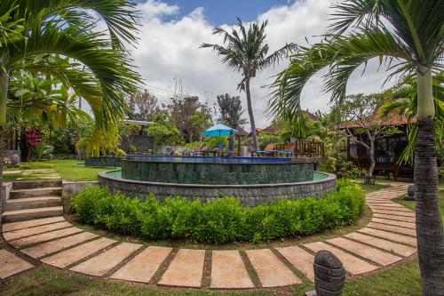 a garden with a fountain with palm trees in the background at Pondooks Joglo in Nusa Lembongan