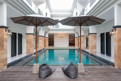 a swimming pool with two umbrellas in a building at Guyana Hotel in Kuta