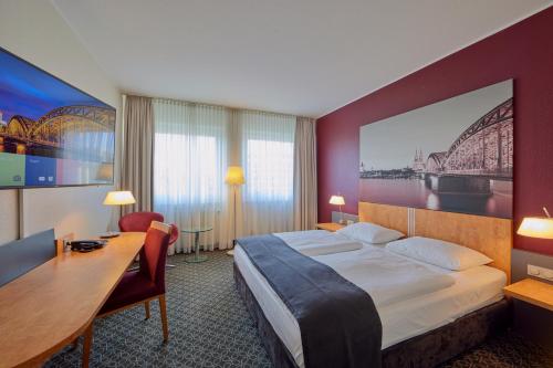 a hotel room with a large bed and a desk at Mercure Hotel Severinshof Köln City in Cologne