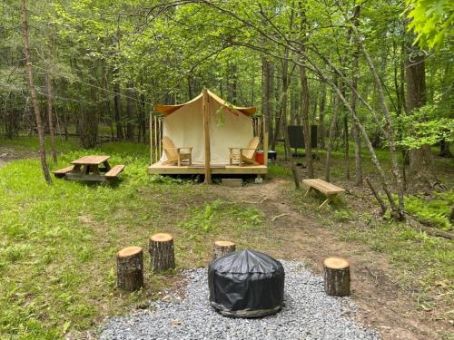 a tent in the woods with a picnic table and benches at Tentrr Signature Site - 6 Ponds Farm Glamping in Morganton