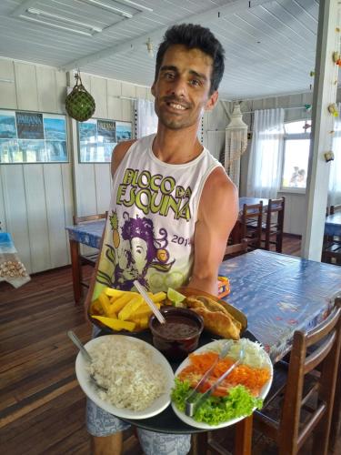 a man holding a plate of food on a table at Pousada Oceano Azul in Ilha do Mel