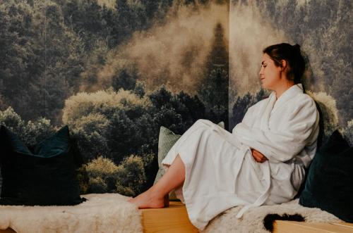 a woman sitting on a bed in front of a painting at Alpenrose Bayrischzell Hotel in Bayrischzell