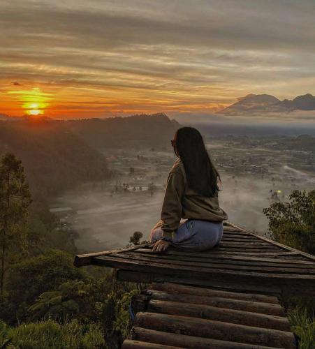 una mujer sentada en la cima de una montaña viendo el amanecer en pinggan sunrise glamping, en Baturaja