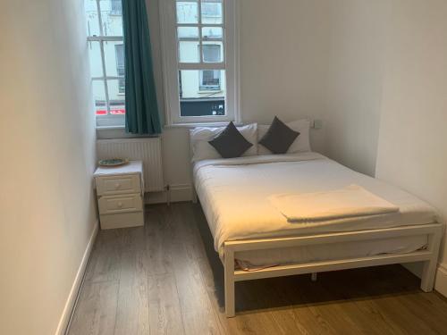 a small bed in a small room with two windows at Brick lane stay in London