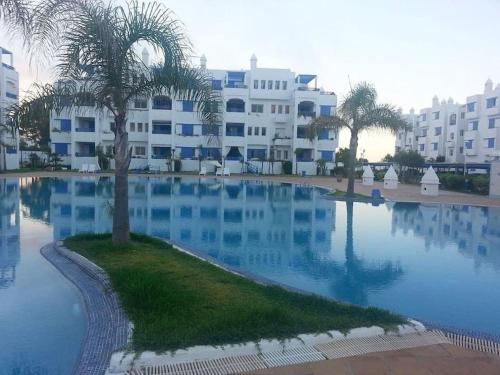 a large swimming pool with a palm tree in front of a building at Superbe appart 3pieces a sania plage MARINA SMIR in M'diq