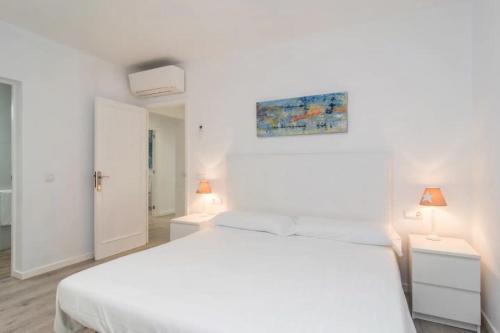 a white bedroom with a white bed and two lamps at Anglesos in Can Picafort