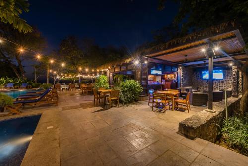 a patio with tables and chairs next to a pool at night at Jet Luxury at Langosta Beach Resort & Villas in Tamarindo