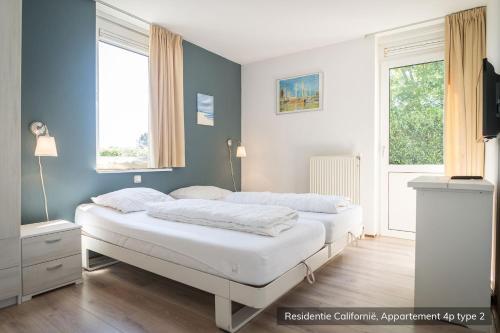 two beds in a room with two windows at Residentie Californië in De Koog