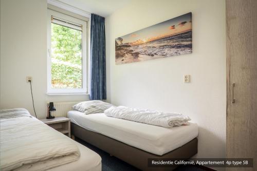 two beds in a room with a picture on the wall at Residentie Californië in De Koog