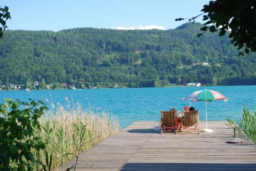 two chairs and a table with an umbrella on a dock at Haus Elisabeth, Appartements in Krumpendorf am Wörthersee