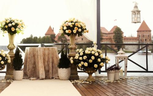a table with flowers in vases on a balcony at Apvalaus Stalo Klubas Gastro & SPA Hotel in Trakai